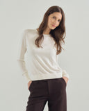 Woman wearing a white sweater and dark pants against a plain background