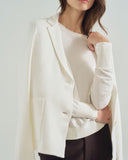Woman wearing a white sweater with a draped design on a plain background