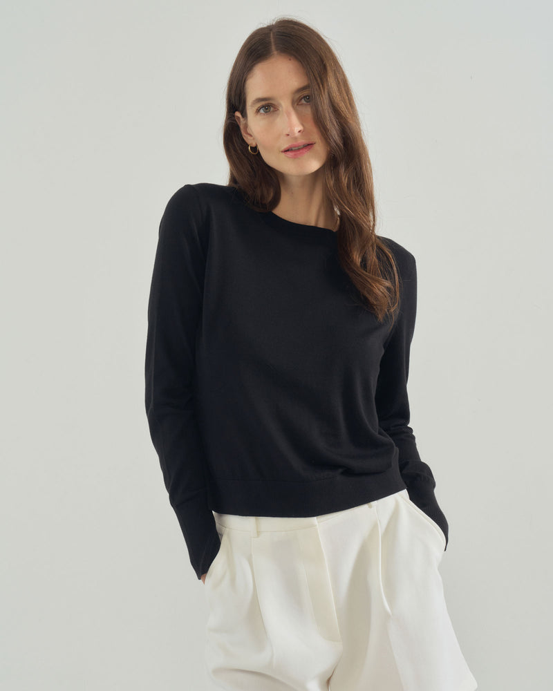 Woman wearing a black sweater and white pants on a plain background