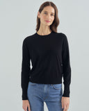 Woman wearing a black sweater and blue jeans against a light gray background