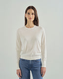 Woman wearing a beige sweater and blue jeans against a plain background