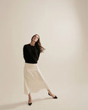 Woman wearing a black top and white skirt against a beige background