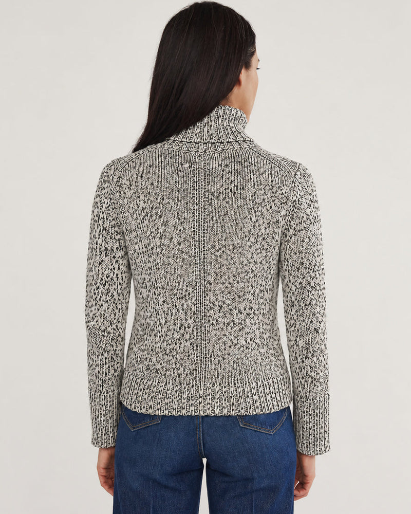 A woman viewed from the back wearing a cropped, long-sleeve knit sweater with a black and white abstract pattern, paired with blue jeans, against a plain light gray studio background.